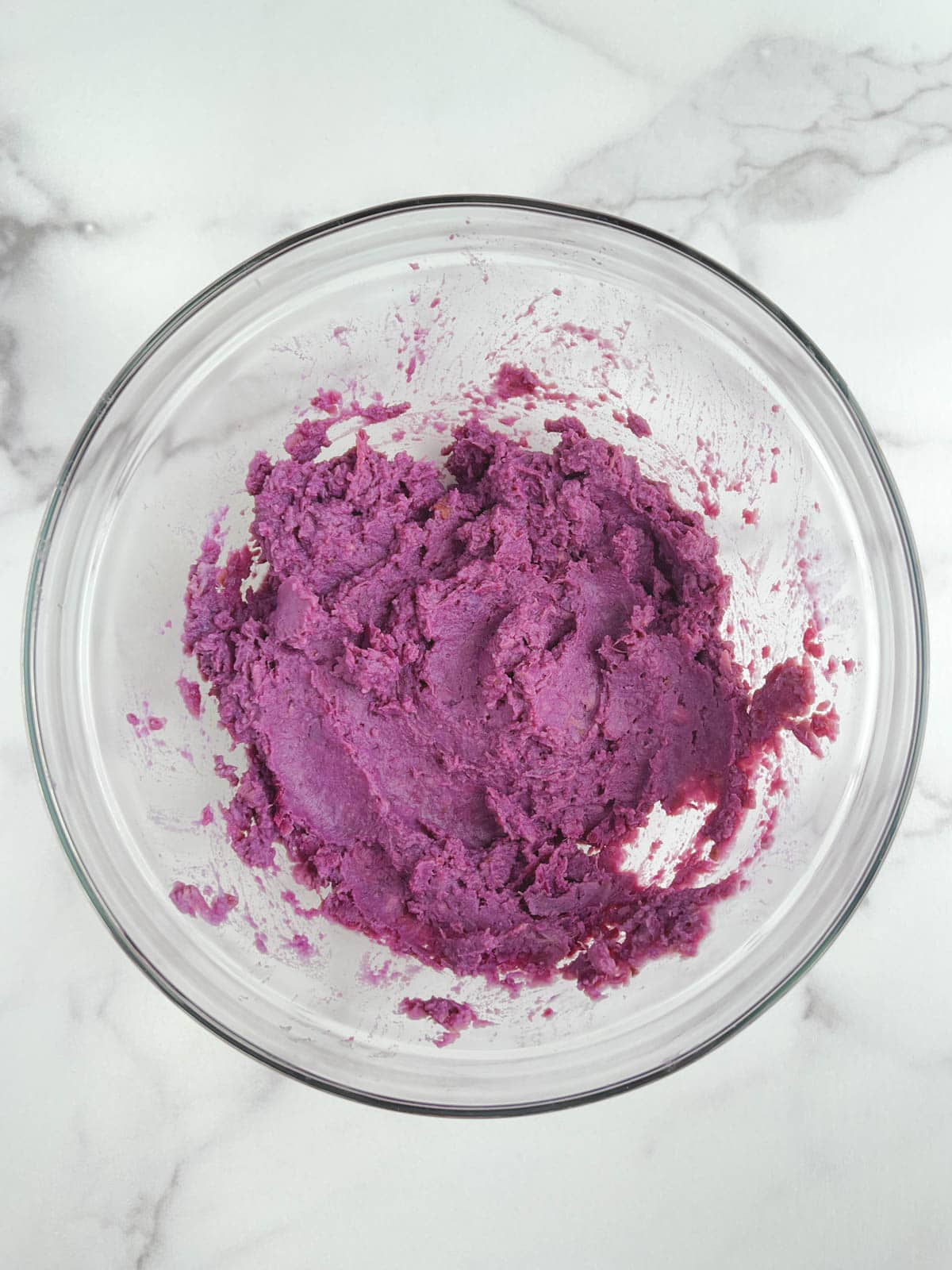 glass bowl containing mashed purple potatoes on a marble background