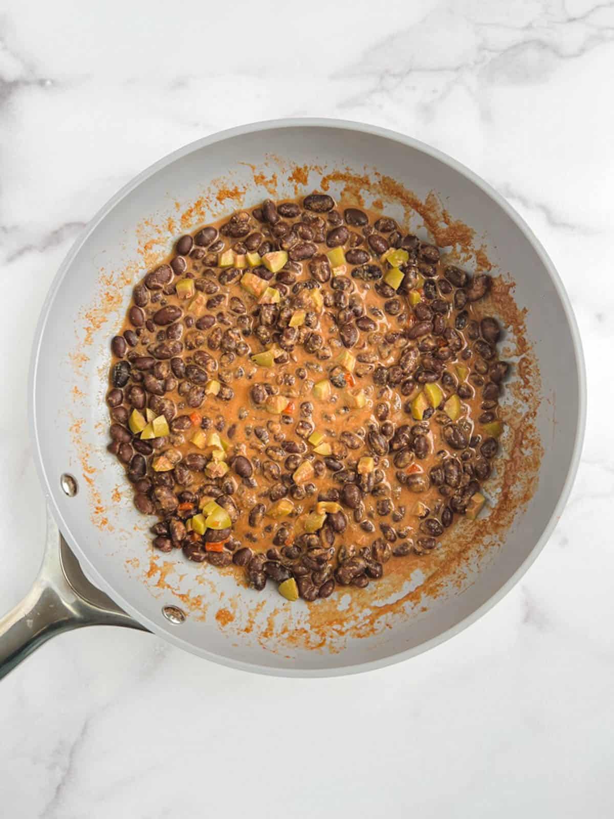 overhead view of skillet containing spicy black beans with sauce and olives added 