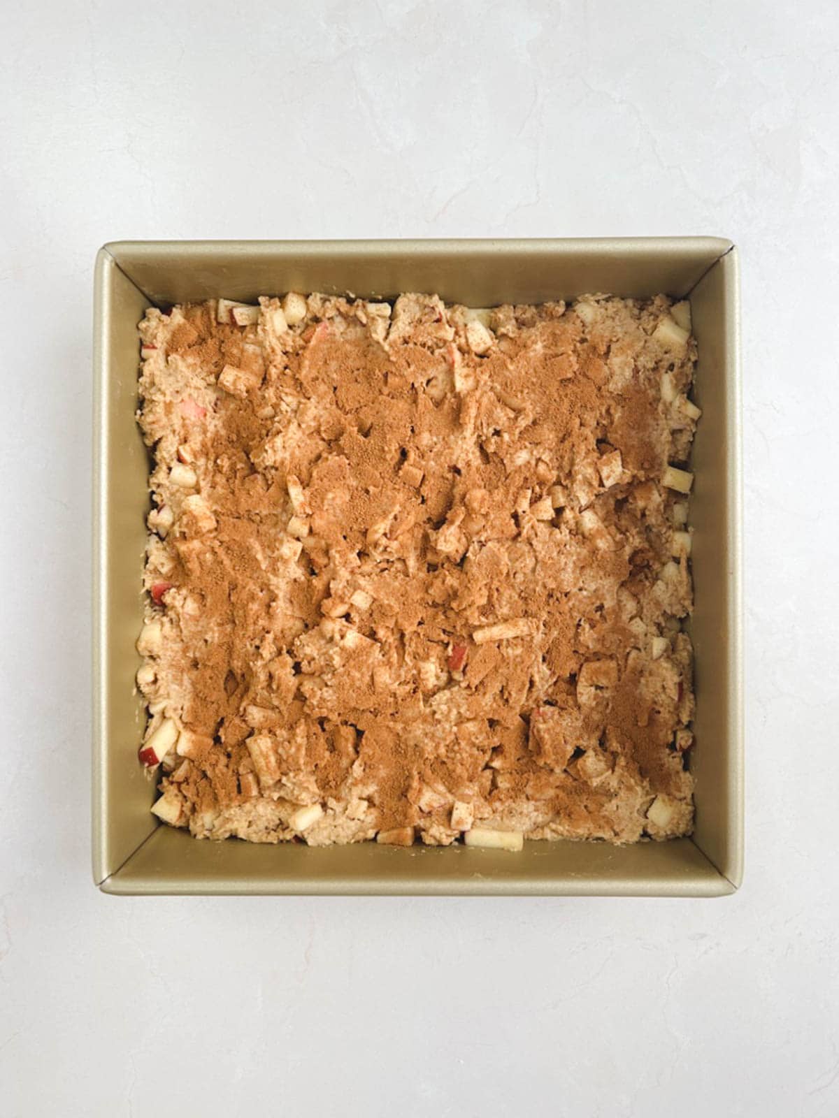 overhead view of a gold square baking pan containing batter for apple coffee cake topped with cinnamon and sugar