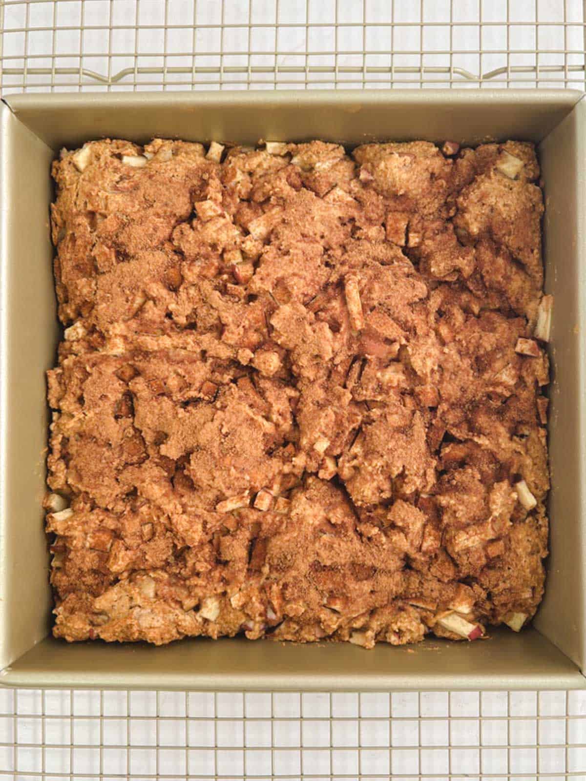 overhead view of a gold square baking pan containing baked apple coffee cake cooling on a wire rack