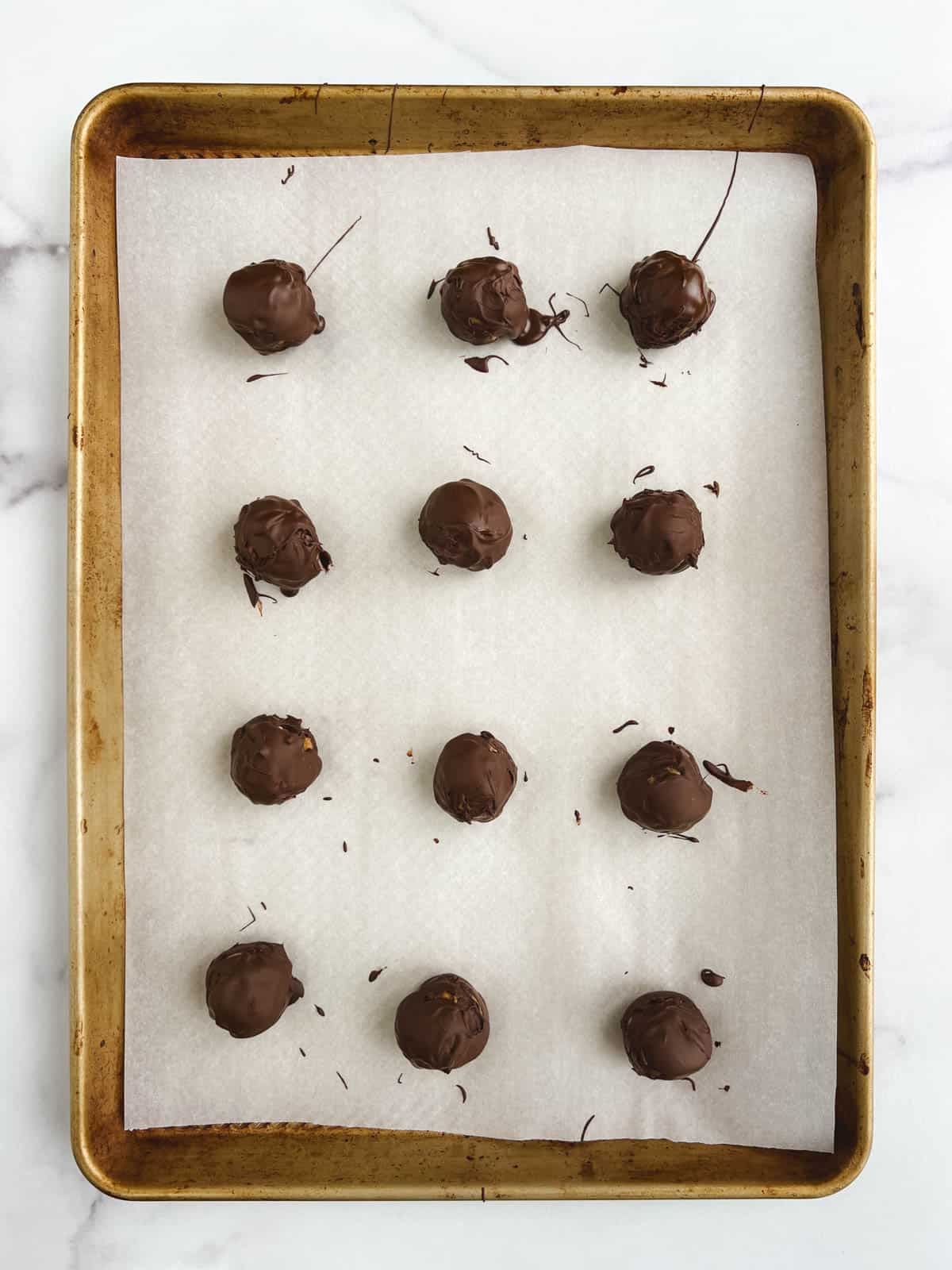 overhead view of prepared baking sheet containing 12 no bake chocolate peanut butter balls covered in chocolate