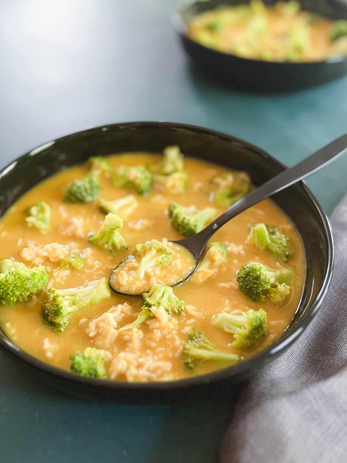 closeup of black bowl containing vegan broccoli cheddar soup with a spoon in it