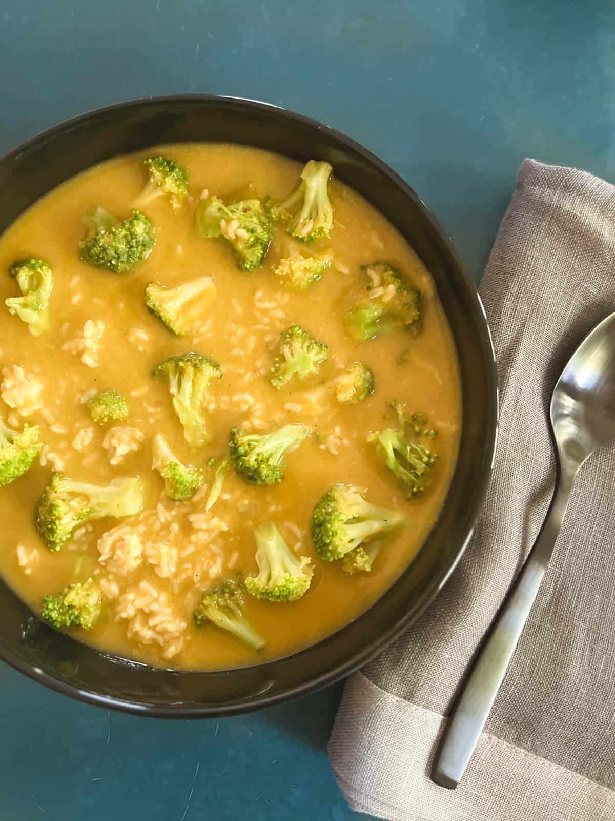 overhead view of black bowl containing vegan broccoli cheddar soup next to a gray linen napkin and spoon