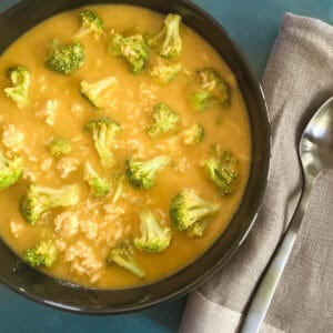 black bowl containing vegan broccoli cheddar soup next to a gray napkin and spoon