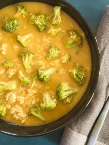 black bowl containing vegan broccoli cheddar soup next to a gray napkin and spoon