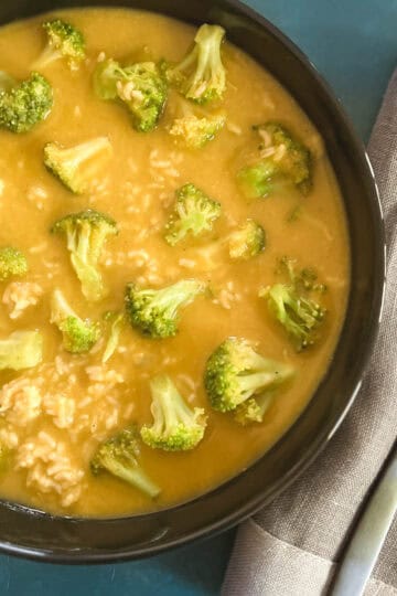 black bowl containing vegan broccoli cheddar soup next to a gray napkin and spoon