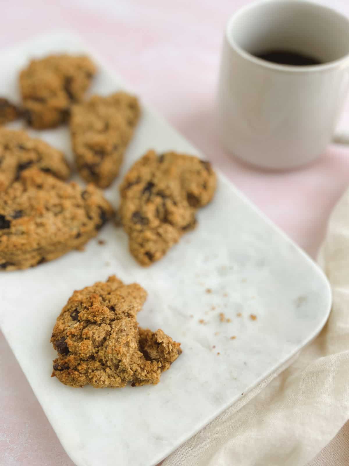 closeup of a chocolate cherry scone with a bite out of it on a marble tray with a coffee mug in the background