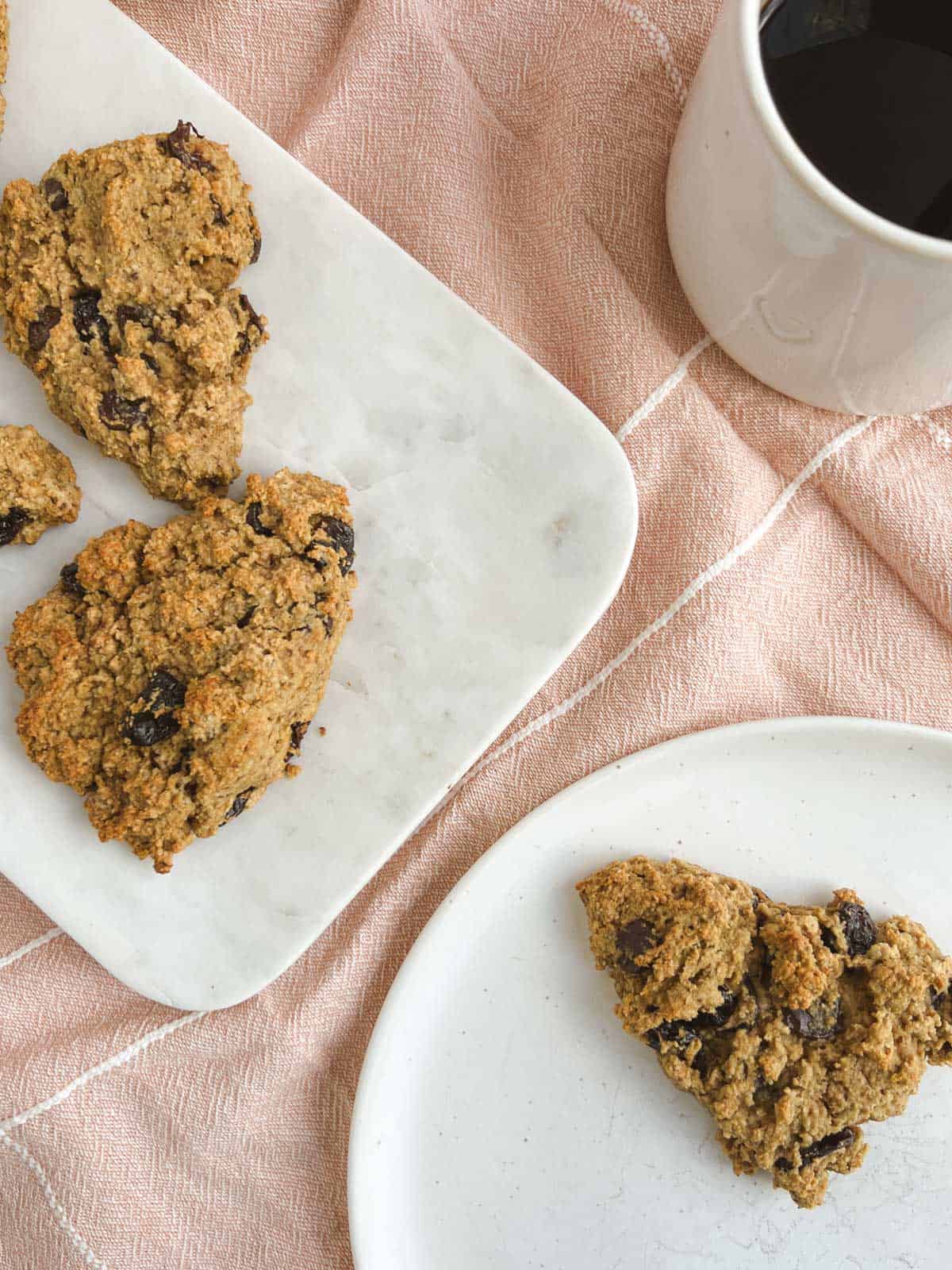 overhead view of chocolate cherry scones on a marble serving tray, a plate with a scone, and a mug of coffee on a light pink cloth