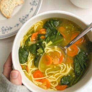 bowl of immunity soup held in hand with a plate of crackers in the background