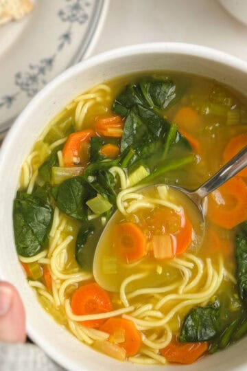 bowl of immunity soup held in hand with a plate of crackers in the background