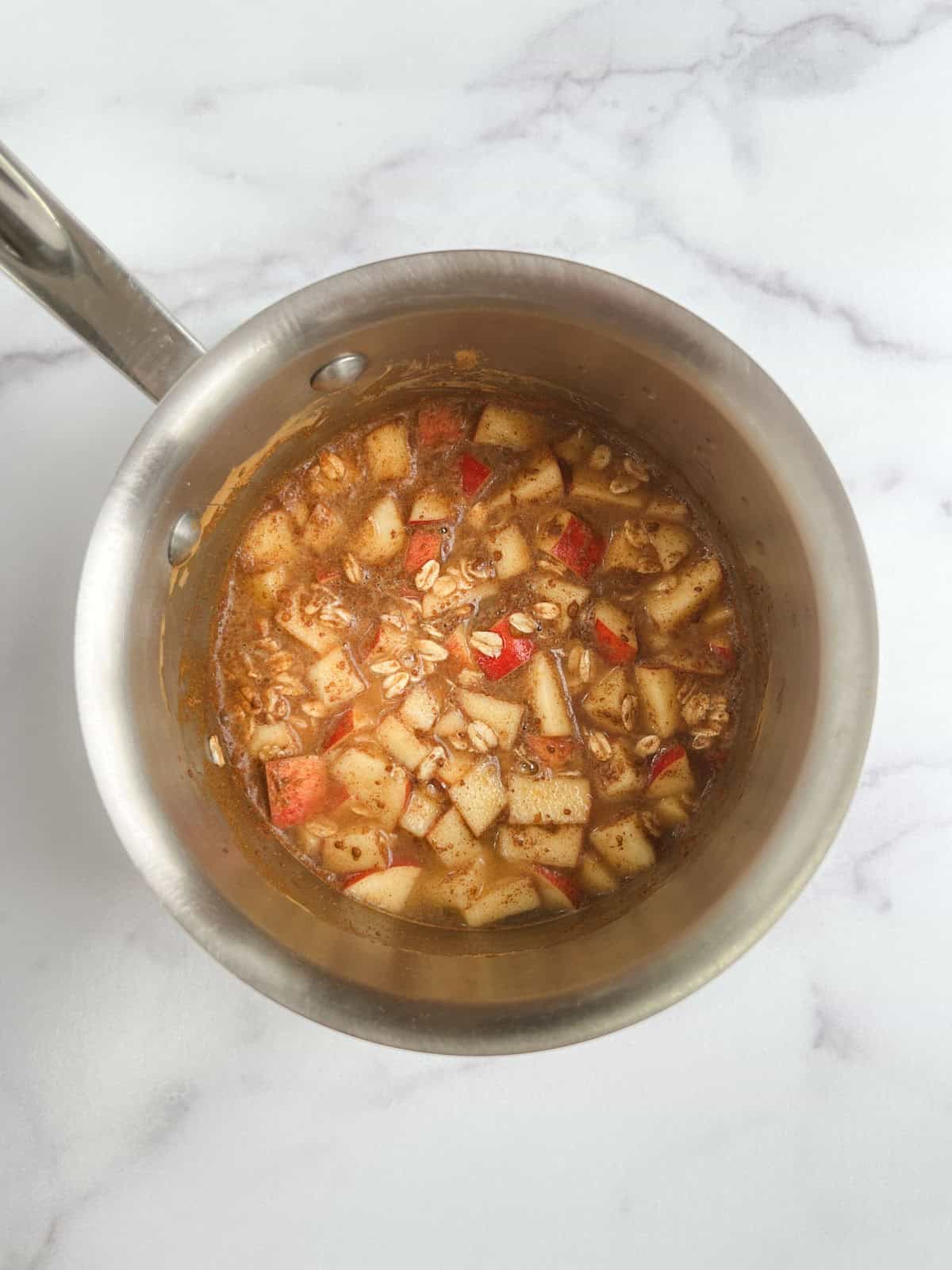 ingredients for one-pot apple cinnamon oatmeal in a stainless steel pot on a marble background