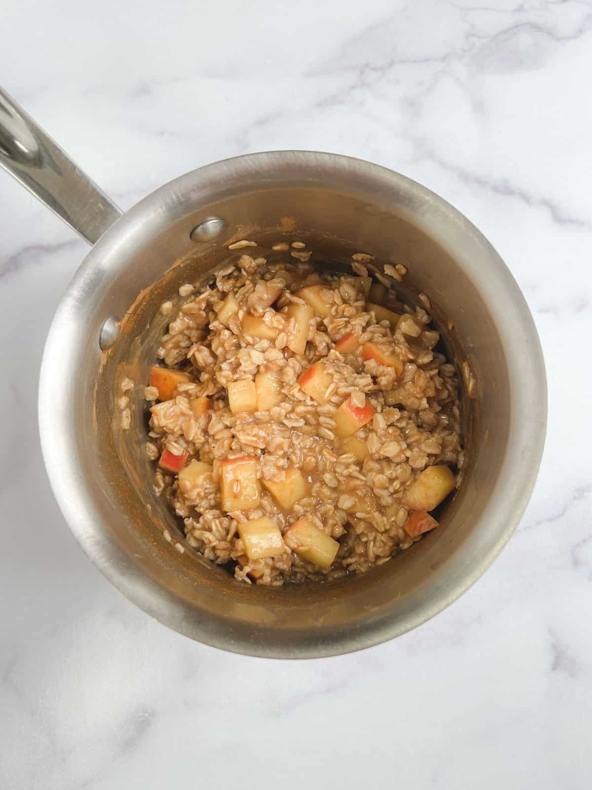 cooked one-pot apple cinnamon oatmeal in a stainless steel pot on a marble background