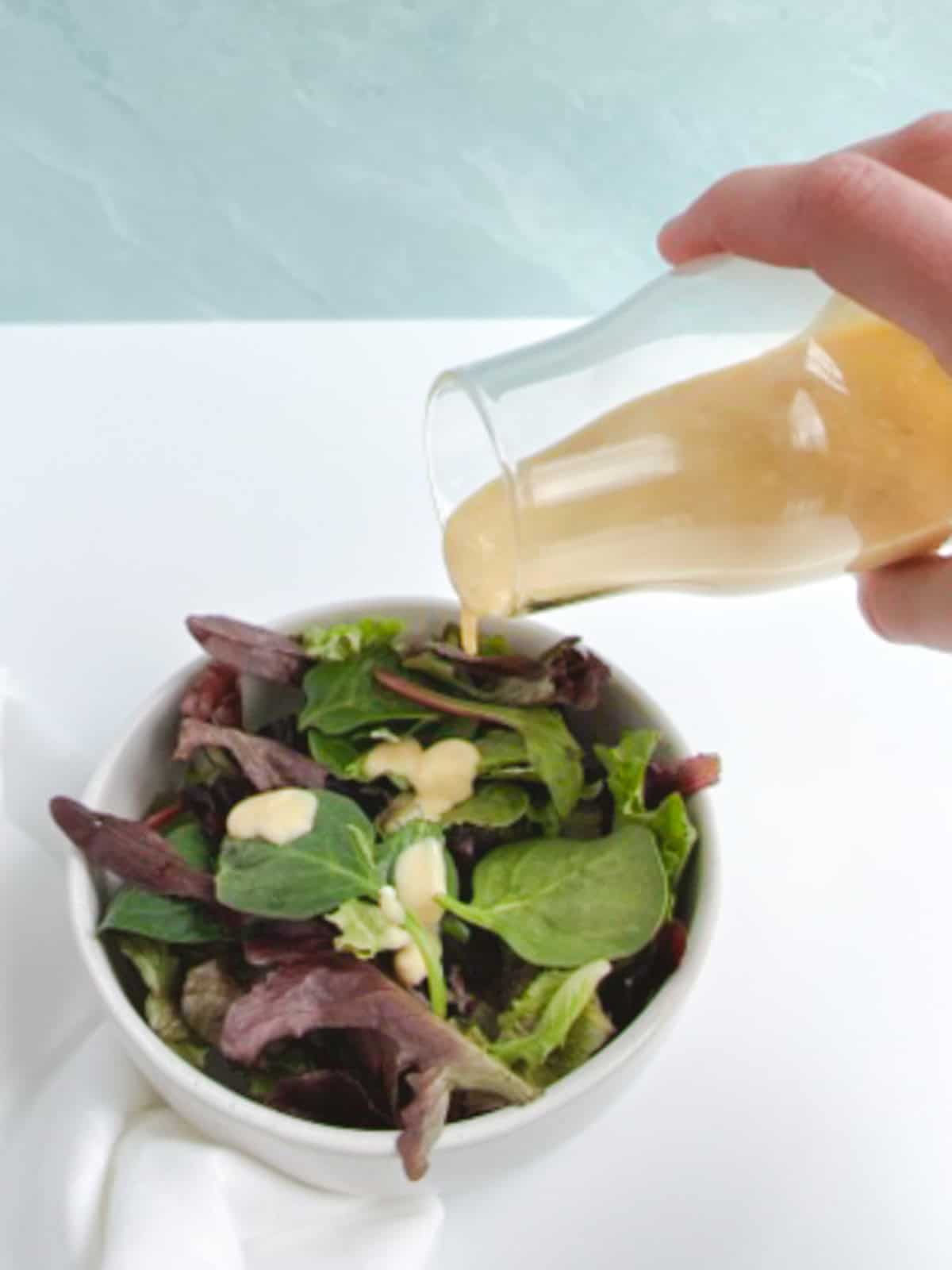 a hand pouring vegan caesar dressing from a glass bottle onto a salad