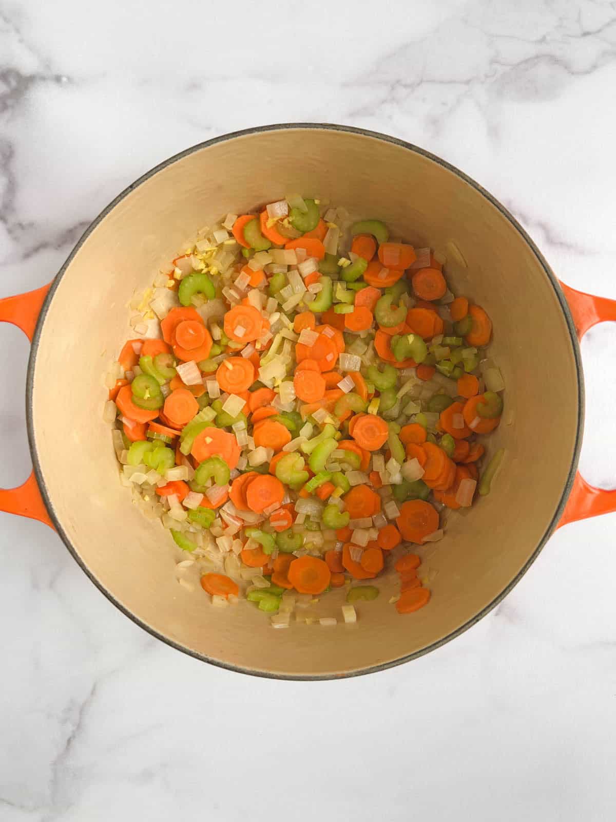 overhead view of Dutch oven containing cooked onions, celery, carrots, and ginger