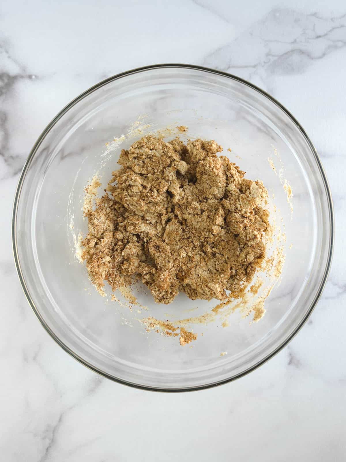 wet and dry ingredients combined in a glass bowl on a white marble background