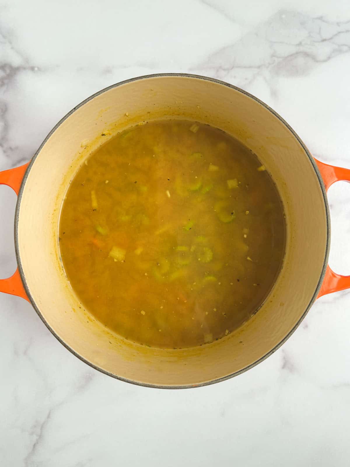 overhead view of Dutch oven containing cooked vegetables with broth added