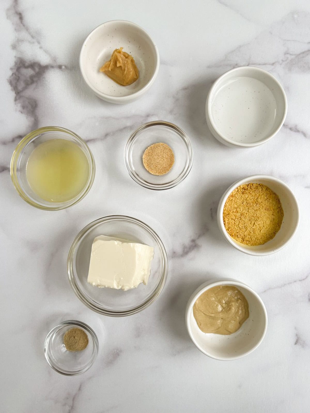 overhead view of bowls of ingredients for vegan caesar dressing on a marble background