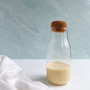 glass bottle of vegan caesar dressing next to a white napkin