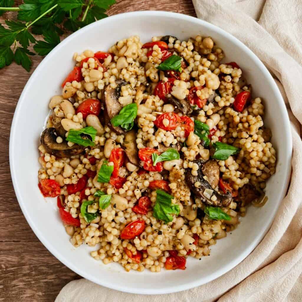 bowl of couscous risotto on a wooden table with a cloth napkin and parsley leaves to the side