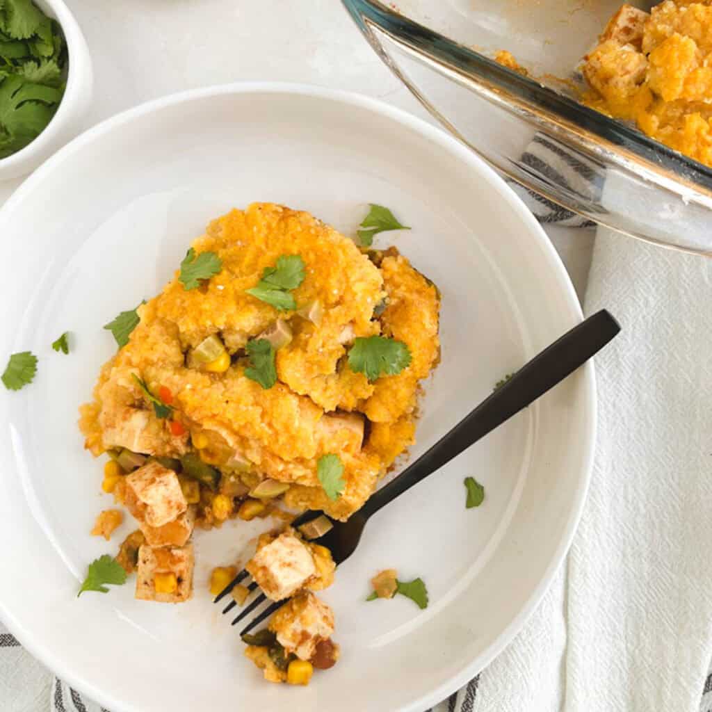 serving of polenta casserole on a dish with a glass casserole dish in the background
