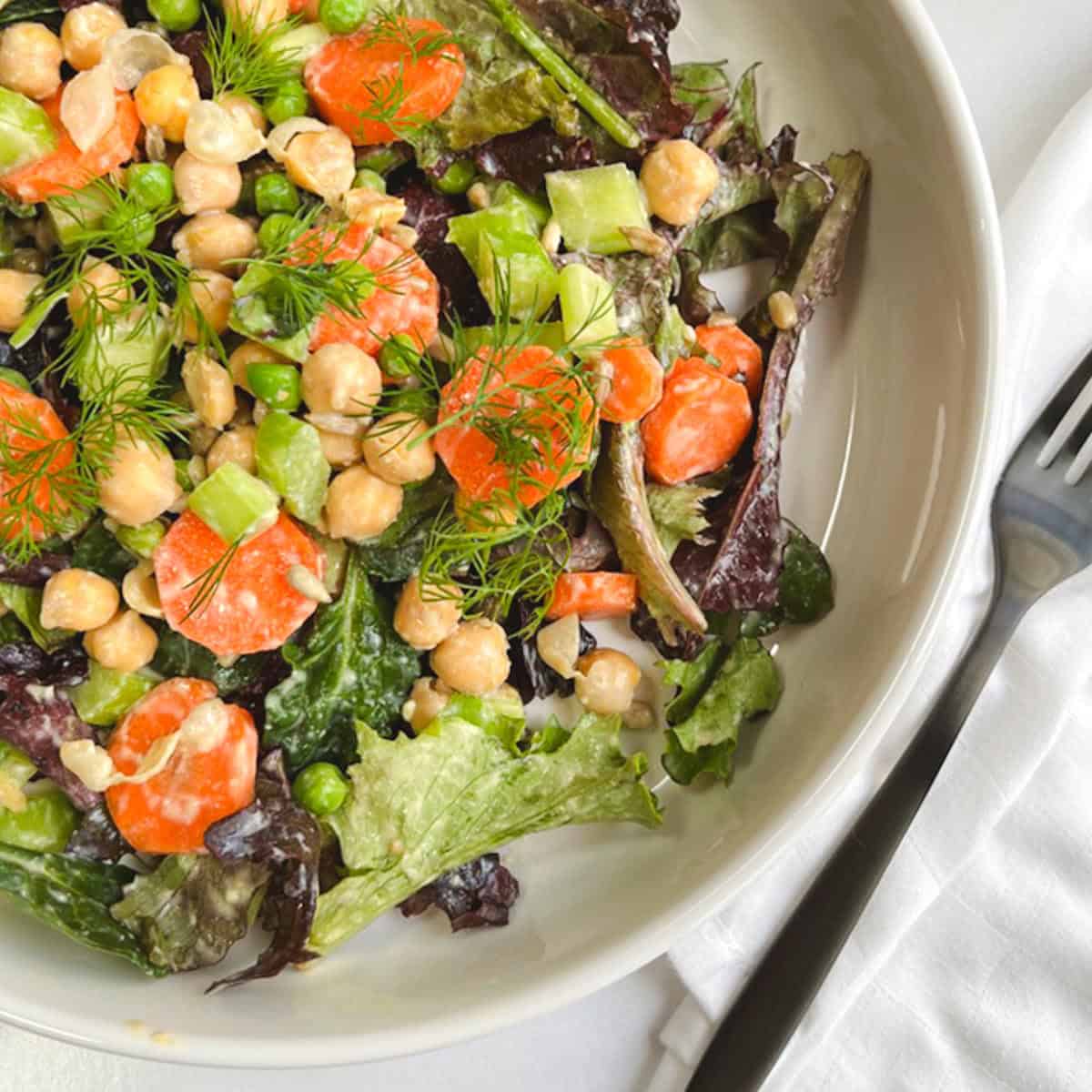 spring salad with vegan Caesar dressing in a white bowl next to a black fork