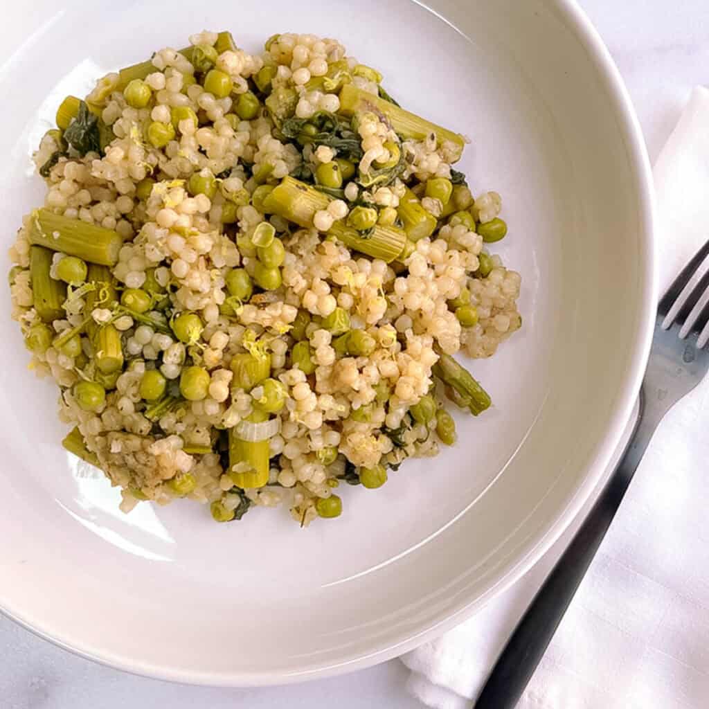 green couscous risotto in a white bowl with a black fork on a marble background