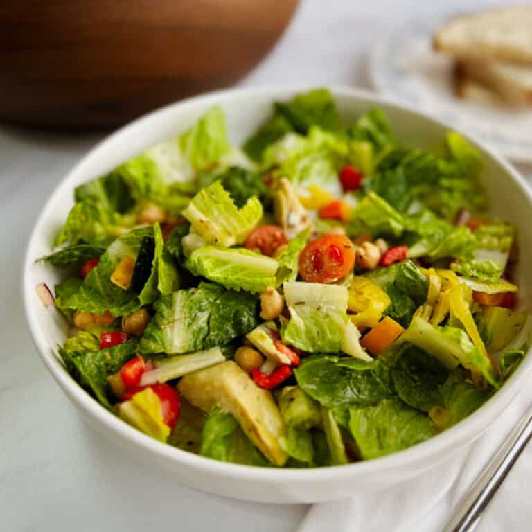 closeup of a bowl of Italian chopped salad with a wooden serving bowl in the background