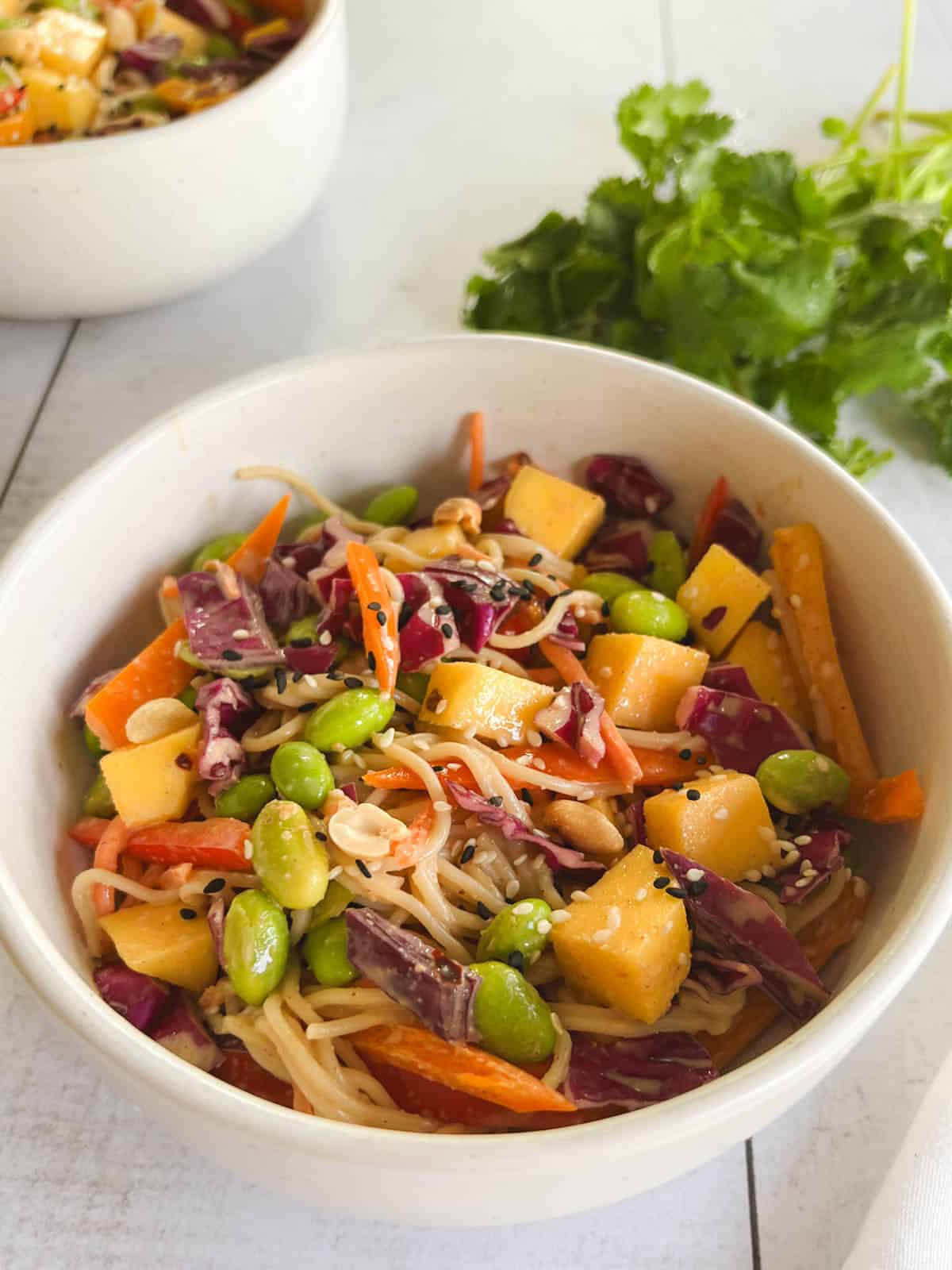 closeup of a serving of mango noodle salad with peanut dressing with cilantro leaves and a serving bowl in the background
