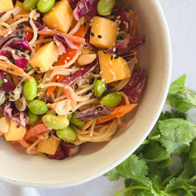 bowl of mango noodle salad with peanut dressing next to fresh cilantro