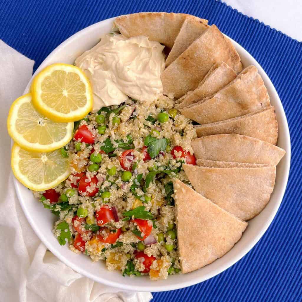 plate of quinoa tabbouleh with a side of hummus, pita wedges, and lemon slices