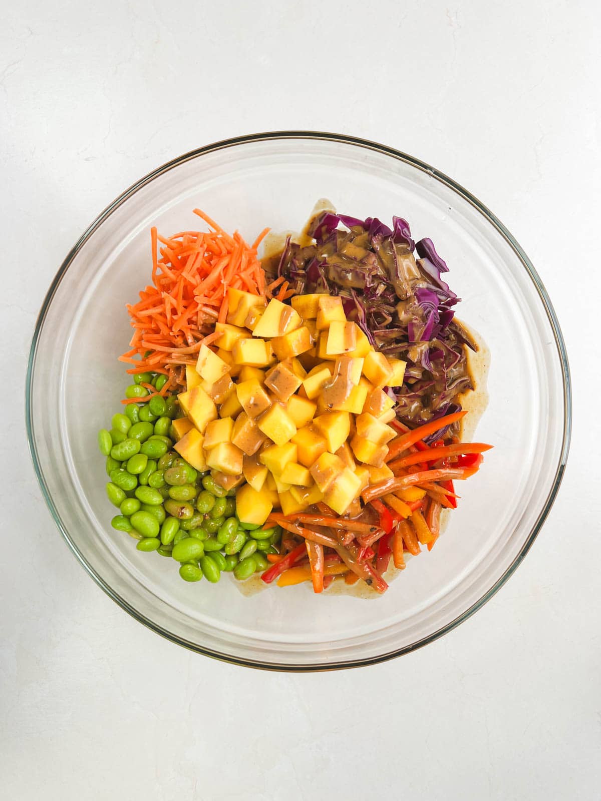 glass bowl containing ingredients for mango noodle salad with peanut dressing added