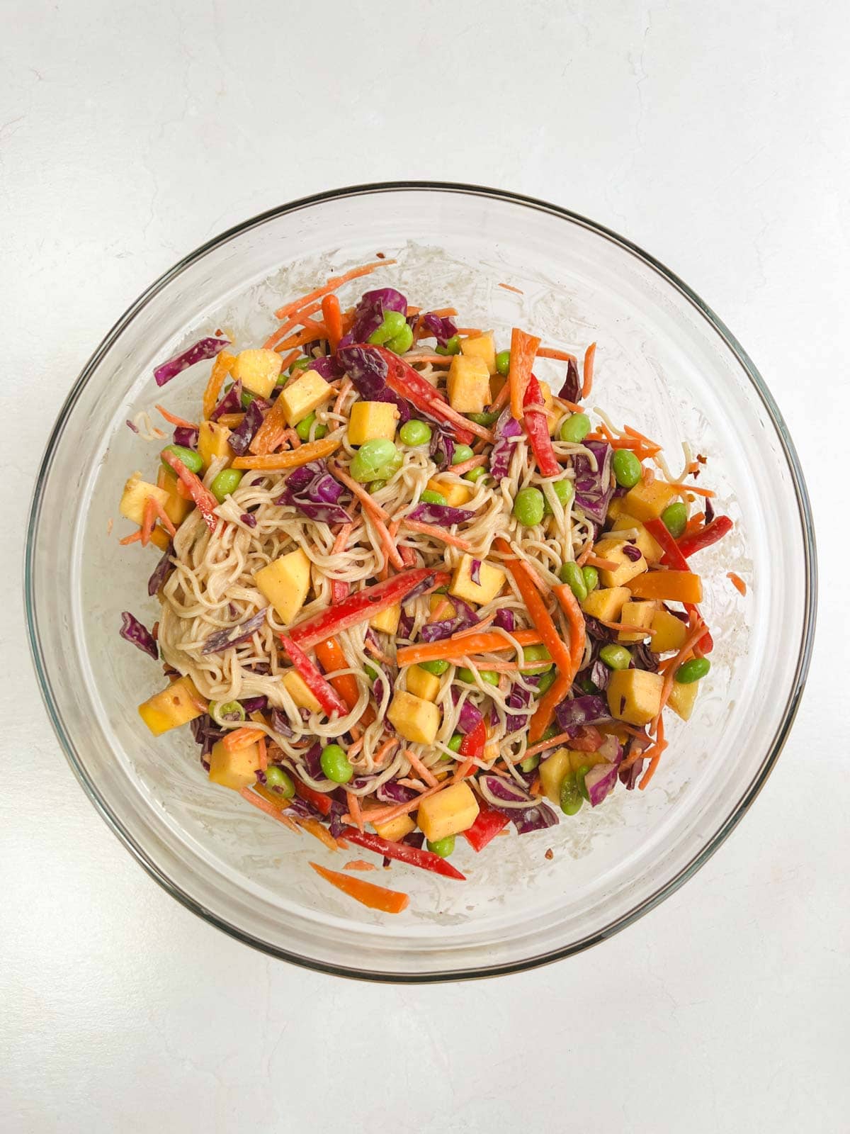 ingredients for mango noodle salad with peanut dressing mixed together in a glass bowl