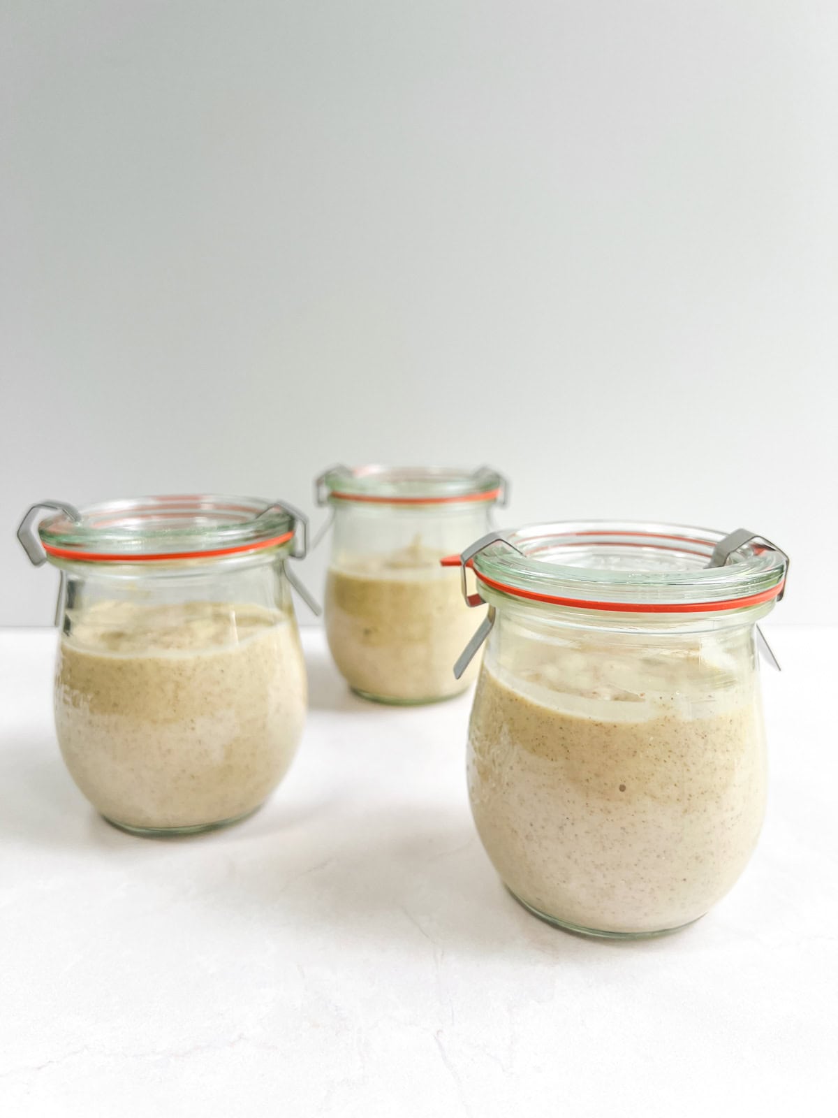 Three jars of mango overnight oats sitting on a white surface