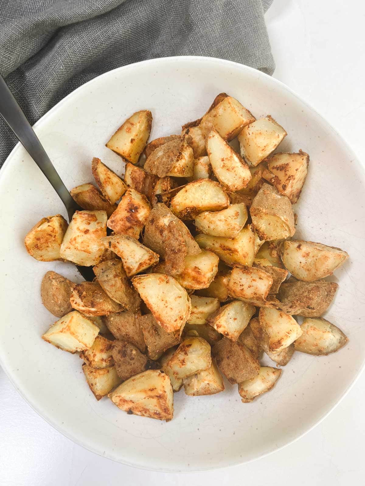 A white bowl with oil-free roasted potatoes and a spoon