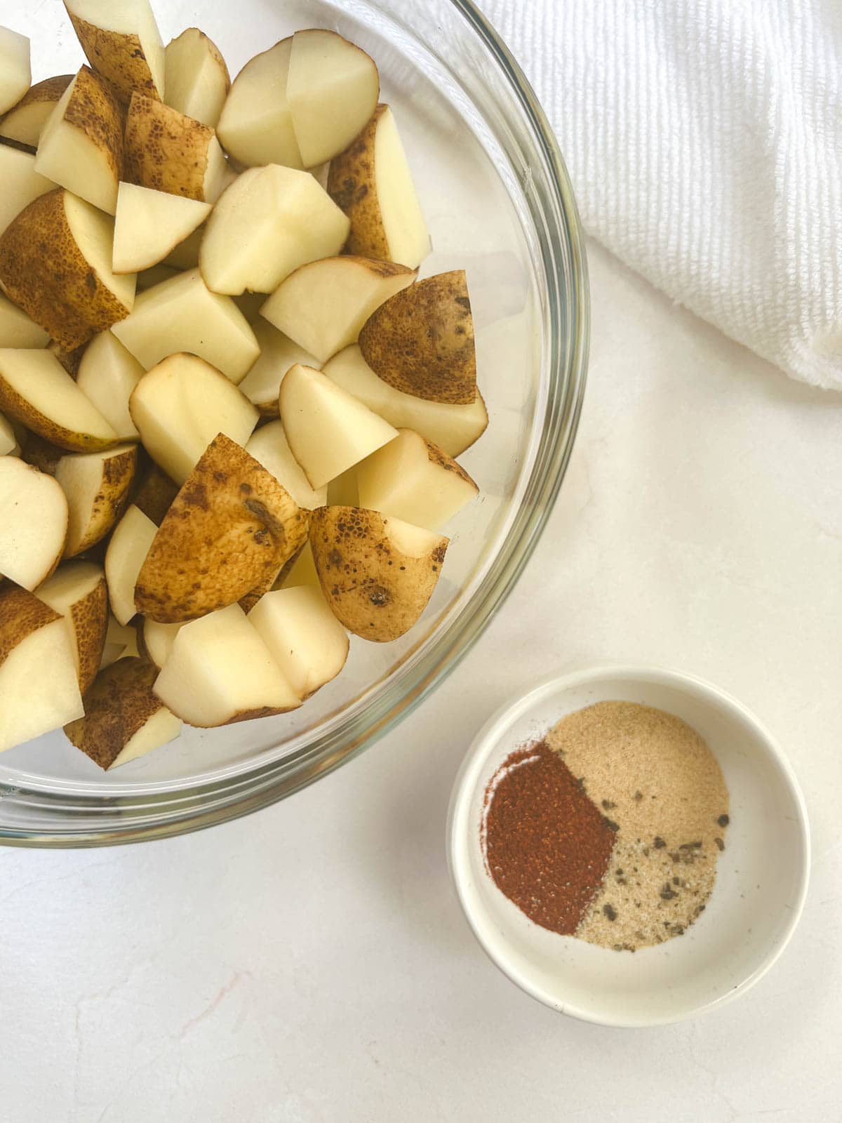 A bowl of diced potatoes next to a bowl of seasoning