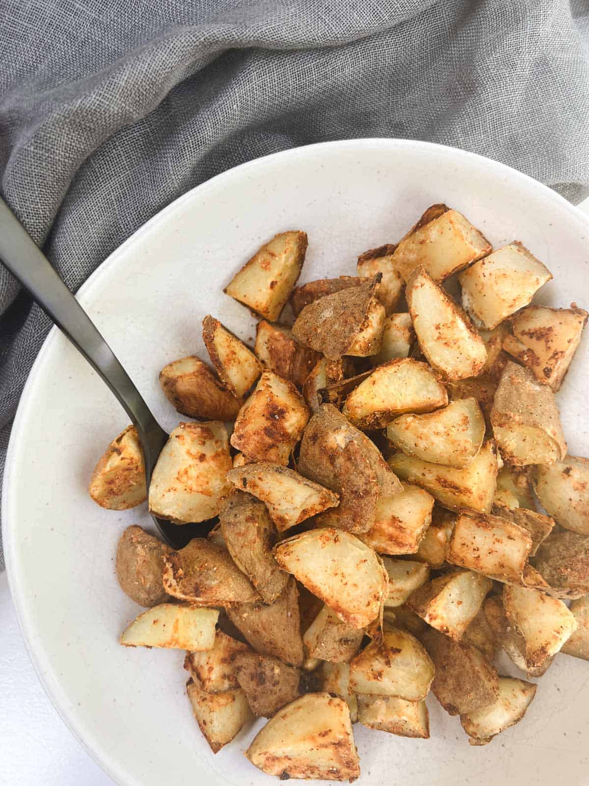 A white bowl filled with oil-free roasted potatoes and a spoon