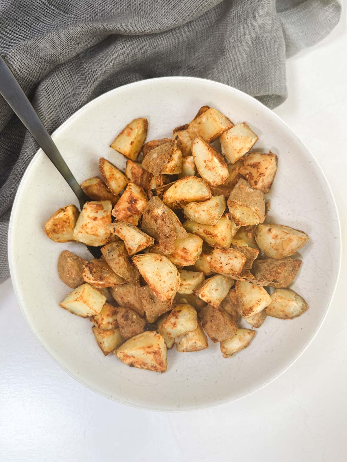 A white bowl filled with oil-free roasted potatoes and a spoon