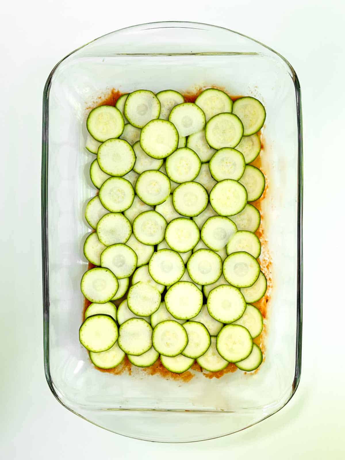 A glass casserole dish filled with sliced zucchini