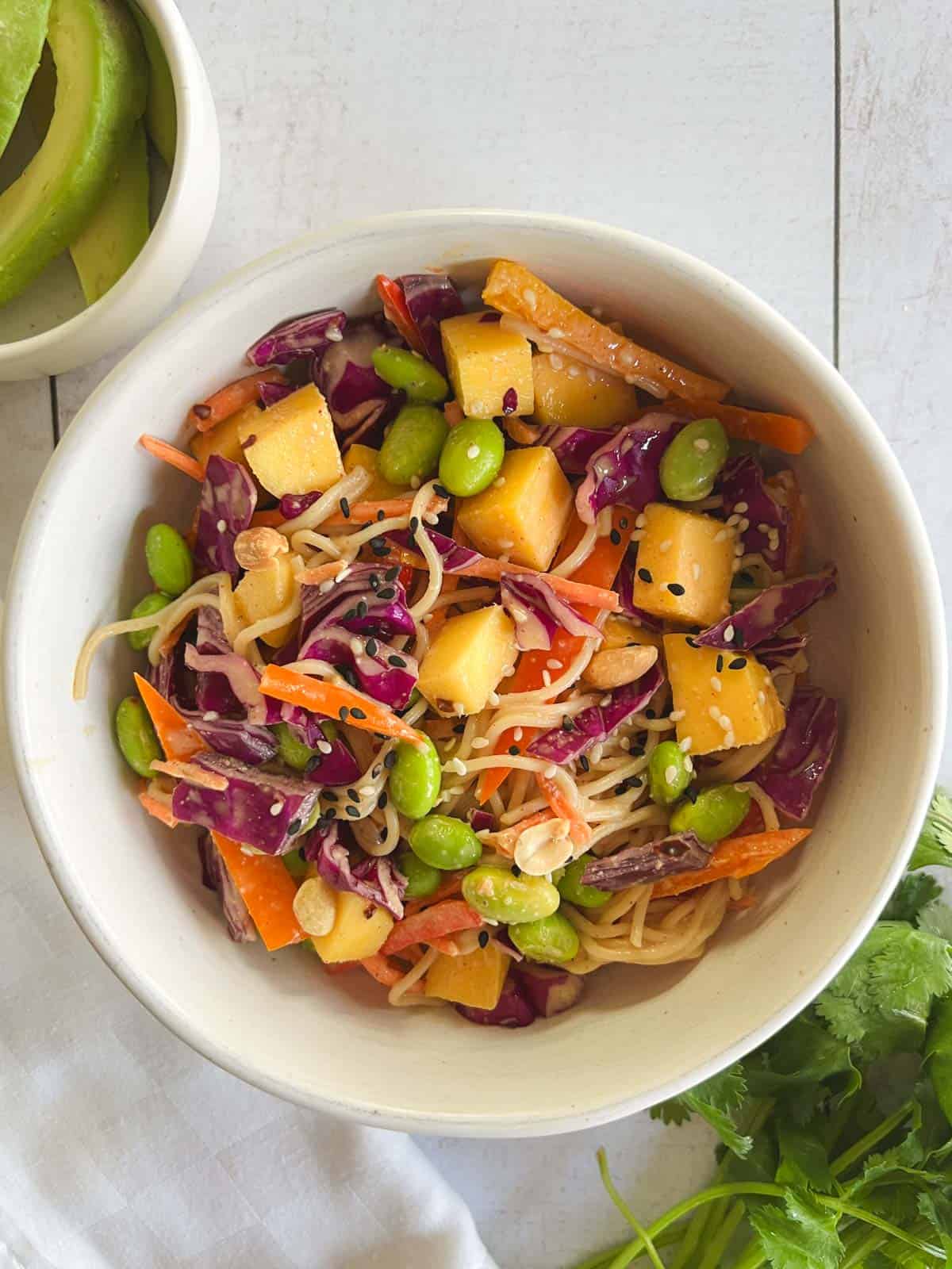 serving bowl of mango noodle salad with peanut dressing with fresh cilantro and avocado slices on the side