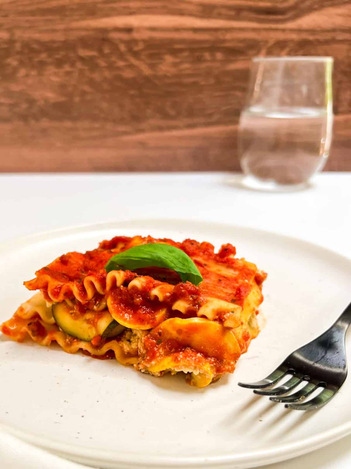 A piece of vegan zucchini lasagna on a white plate with a fork