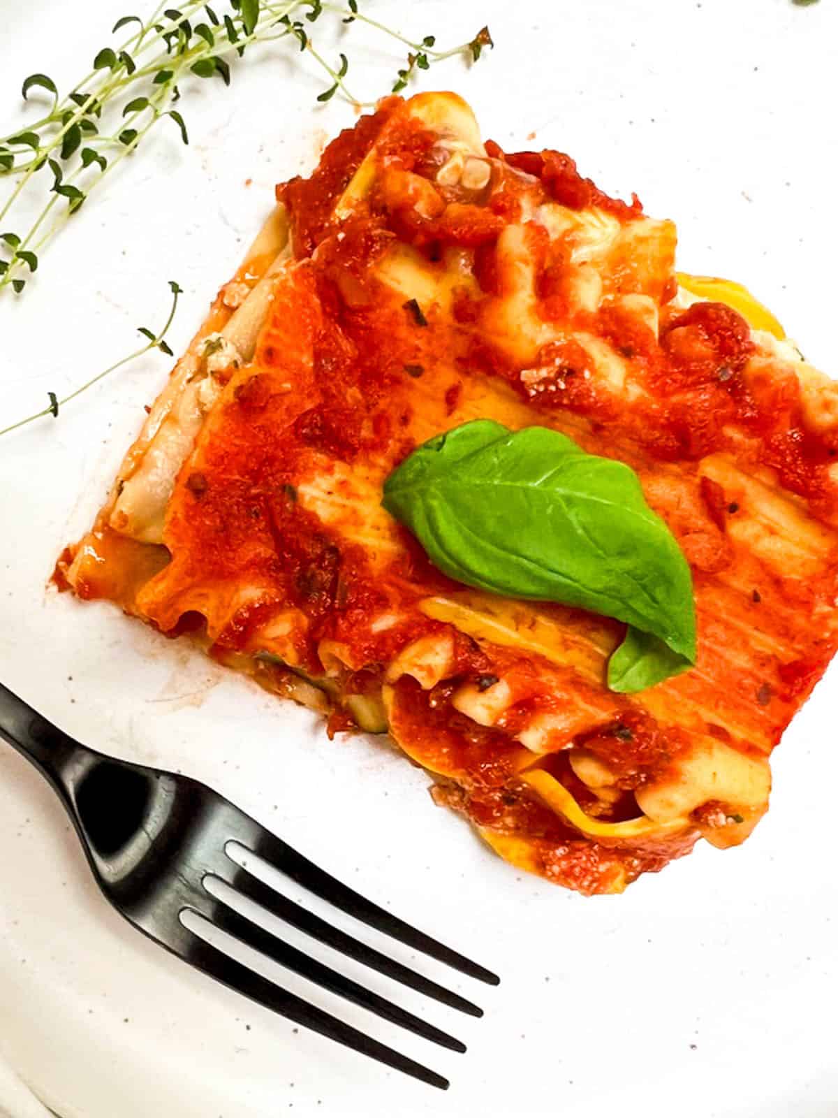 A slice of lasagna with a basil leaf on a white plate