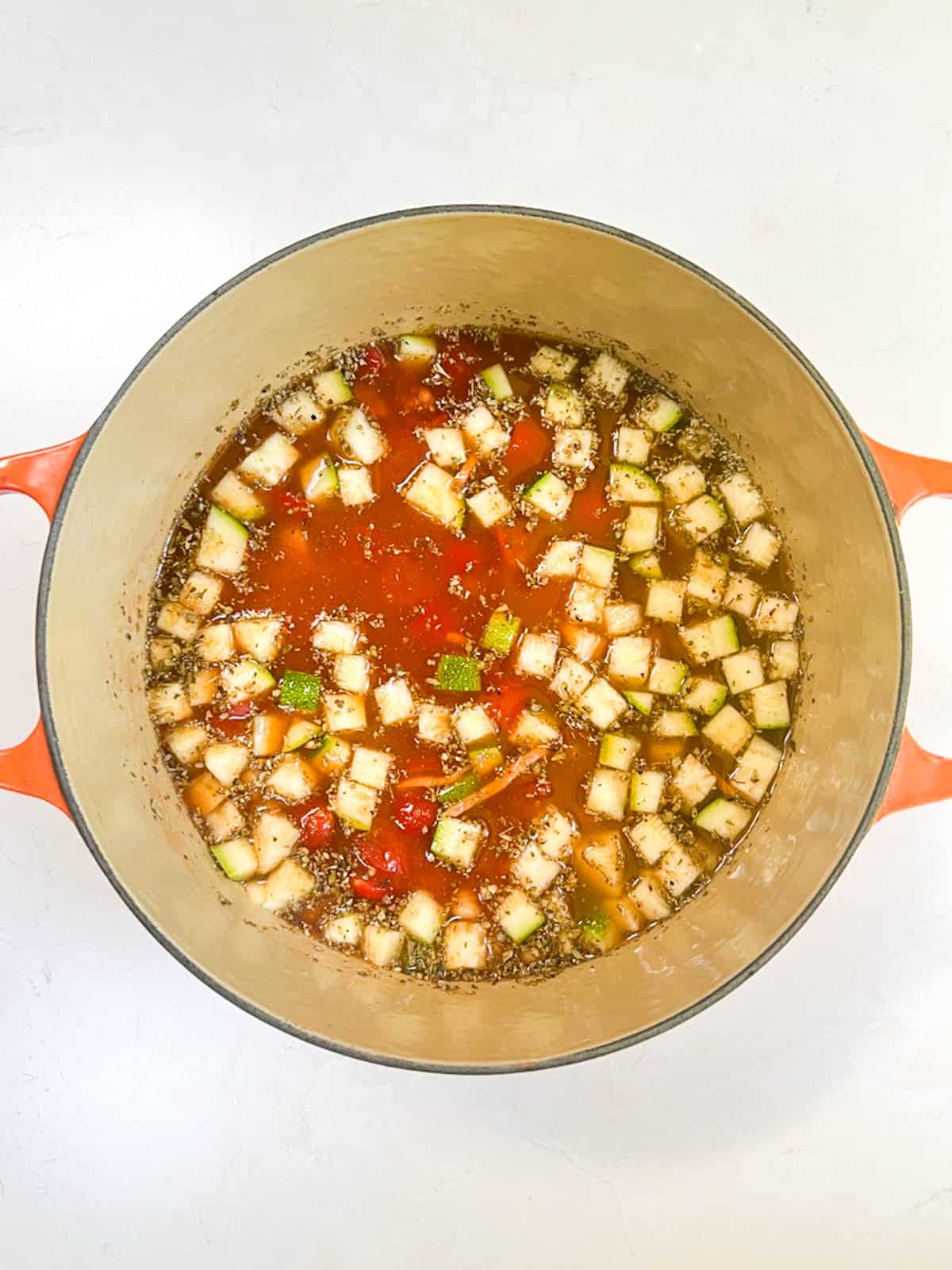 A pot filled with minestrone soup ingredients on a white surface.