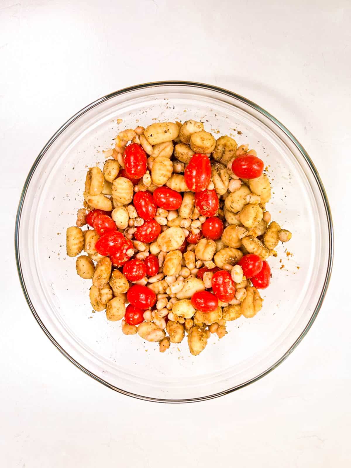 A bowl filled with beans, gnocchi, tomatoes, and spices.