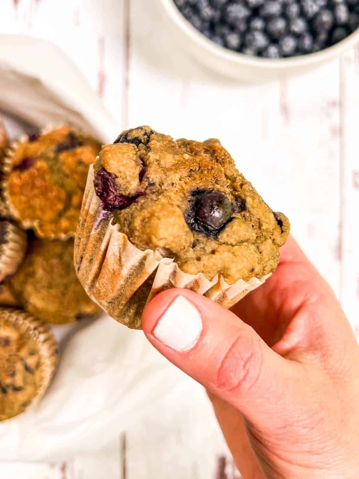 A person holding a muffin with blueberries.