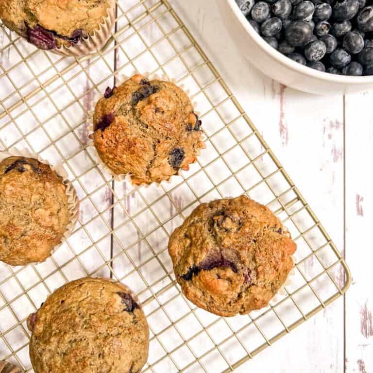 Blueberry muffins on a cooling rack with blueberries.