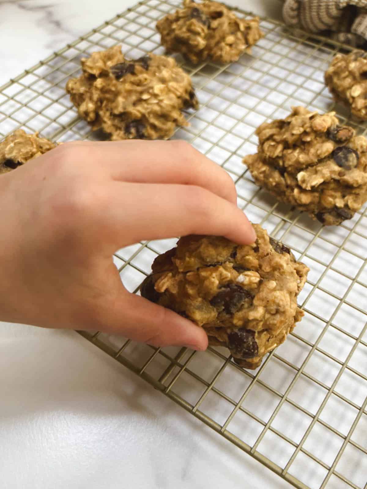 A hand reaching for a cookie on a cooling rack.