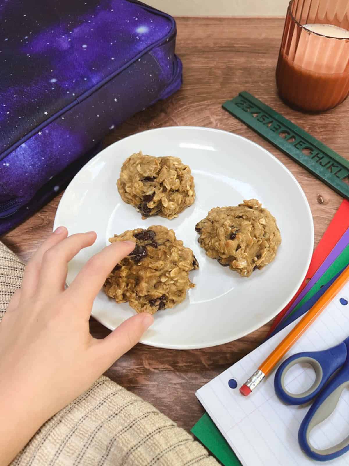 A child's hand reaching for a plate of cookies on a table.